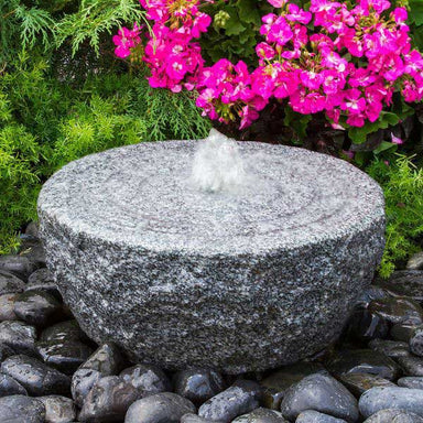 Ringed Circle Fountain on black peebles beside pink flowers